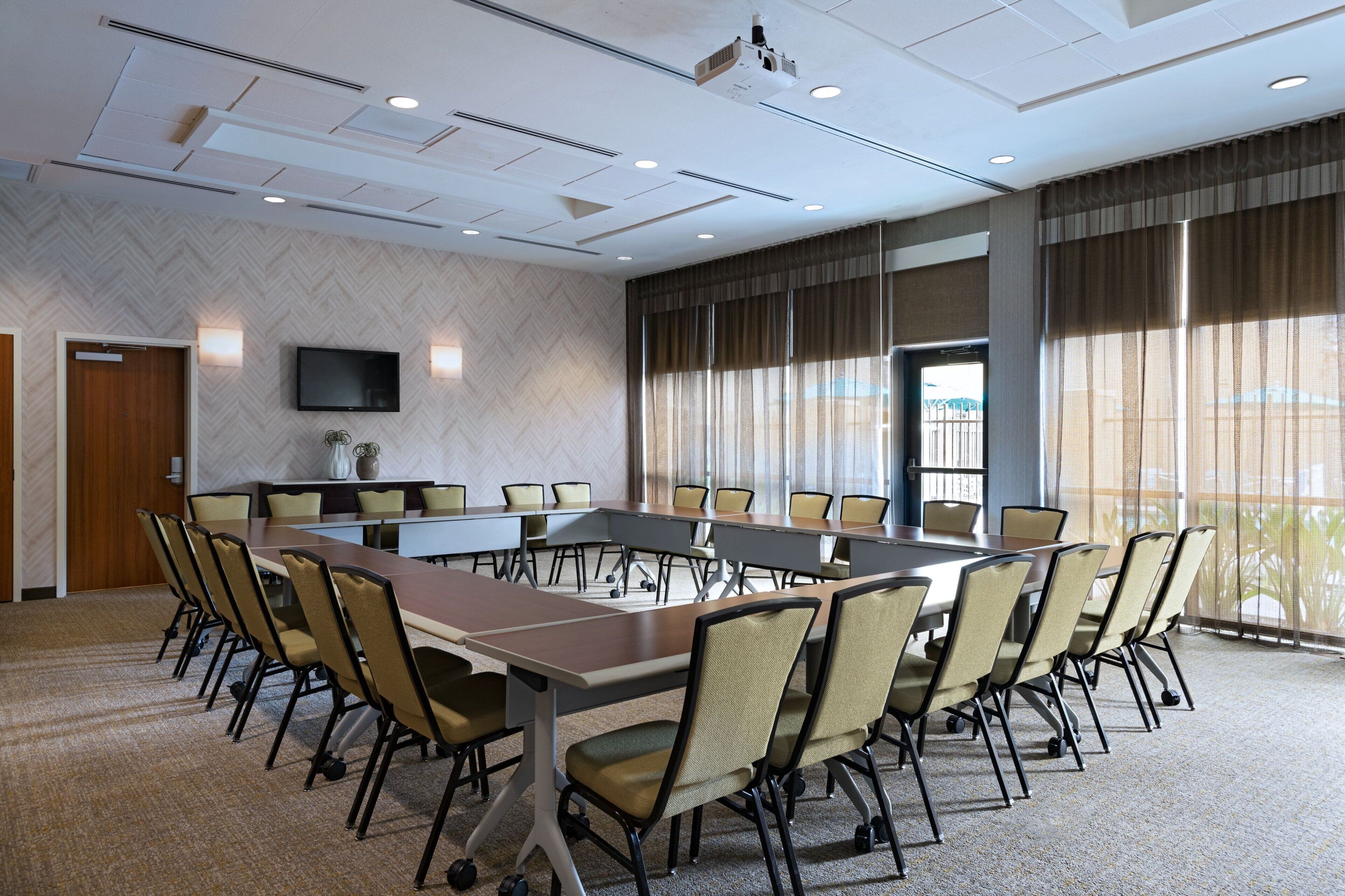 A conference room with a long table, chairs, a television, and a large window with curtains.