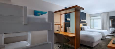 Ein Hotelzimmer mit Etagenbett, Schreibtisch, zwei Einzelbetten, einem großen Spiegel und Blick auf die Stadt.