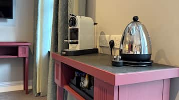 A pink table with a coffee maker, a kettle, and a glass container on a countertop.