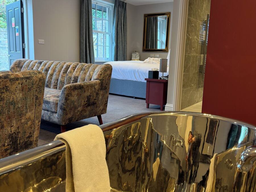 Habitación de hotel con sofá, cama, espejo y una bañera metálica grande.