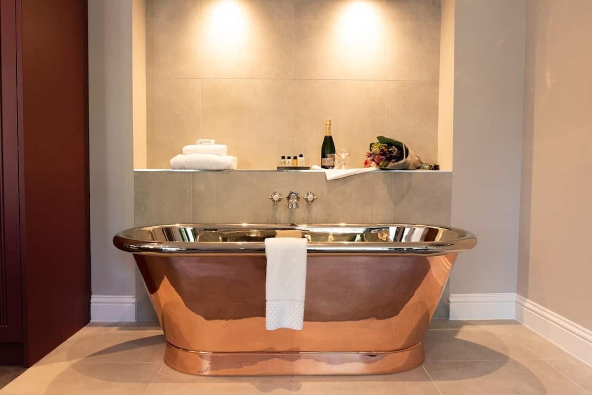 Un baño moderno con una bañera de cobre independiente, un perchero y un estante con artículos de tocador.