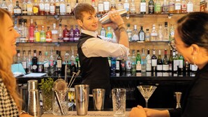 Eine Bar mit einem Barkeeper, der ein Getränk zubereitet, Regalen voller Spirituosen und Barutensilien auf der Theke.