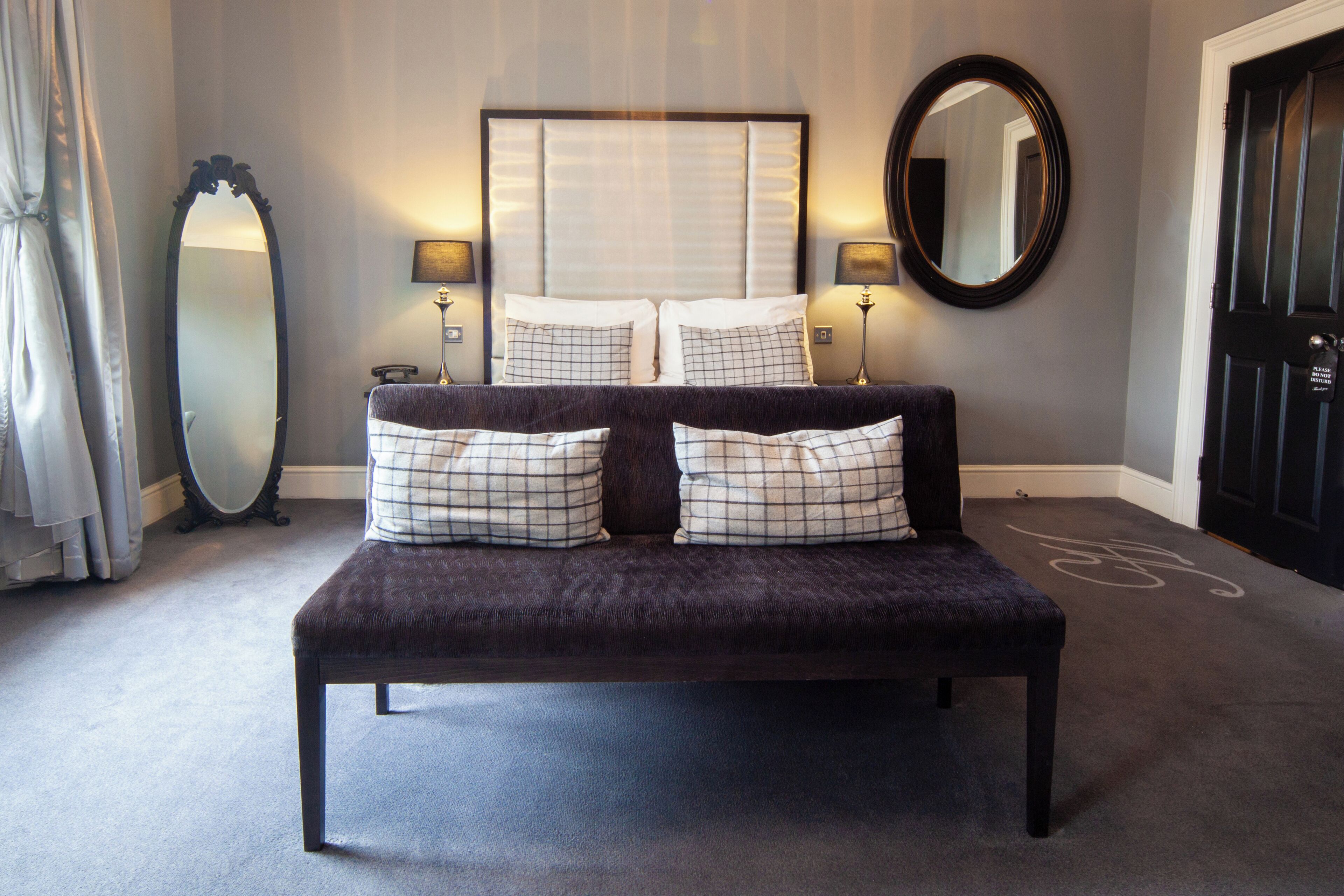 A bedroom with a large bed, two bedside lamps, a mirror, and a door.