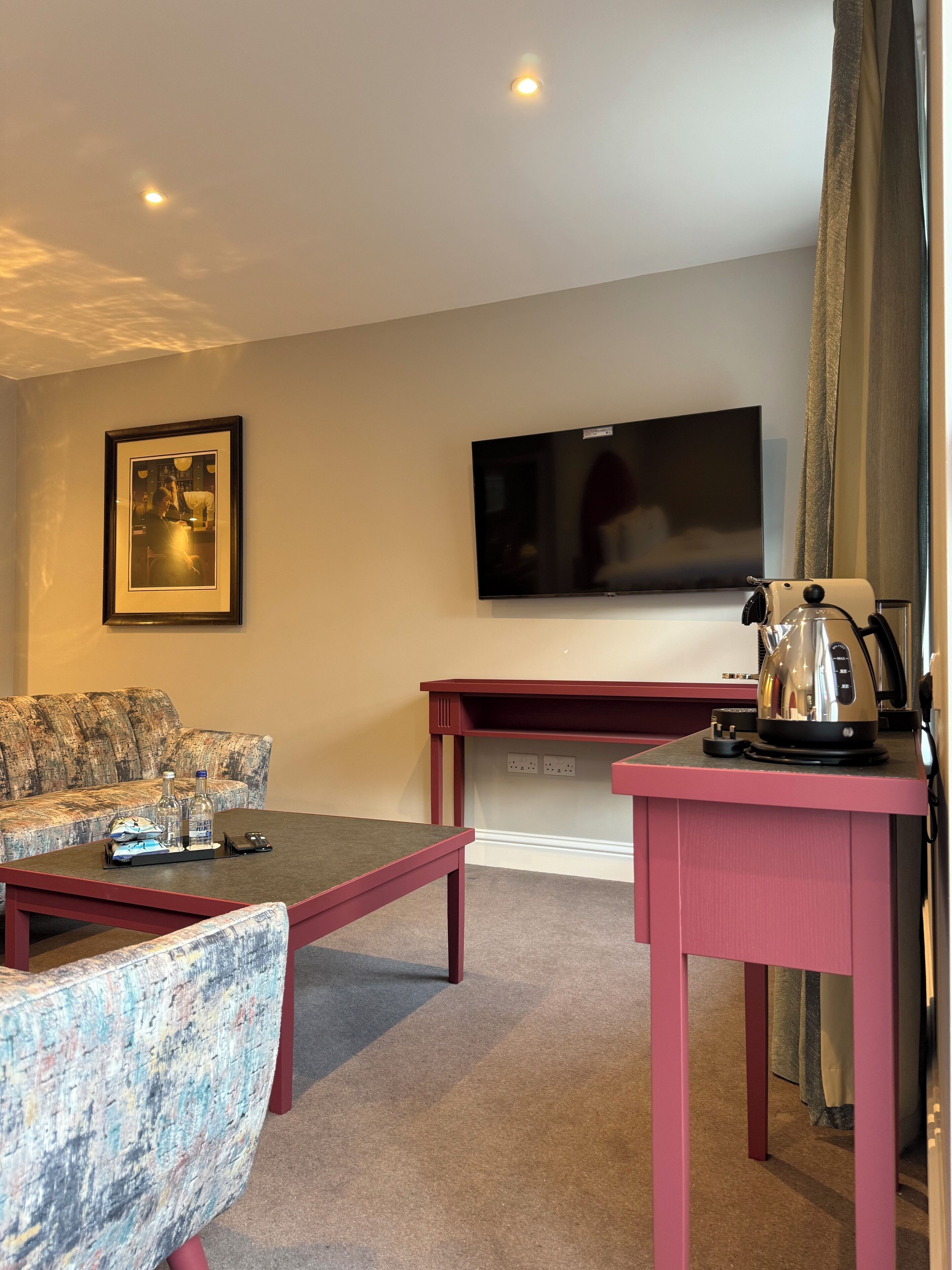 A living room with a sofa, a coffee table, a TV, and a table with a kettle.