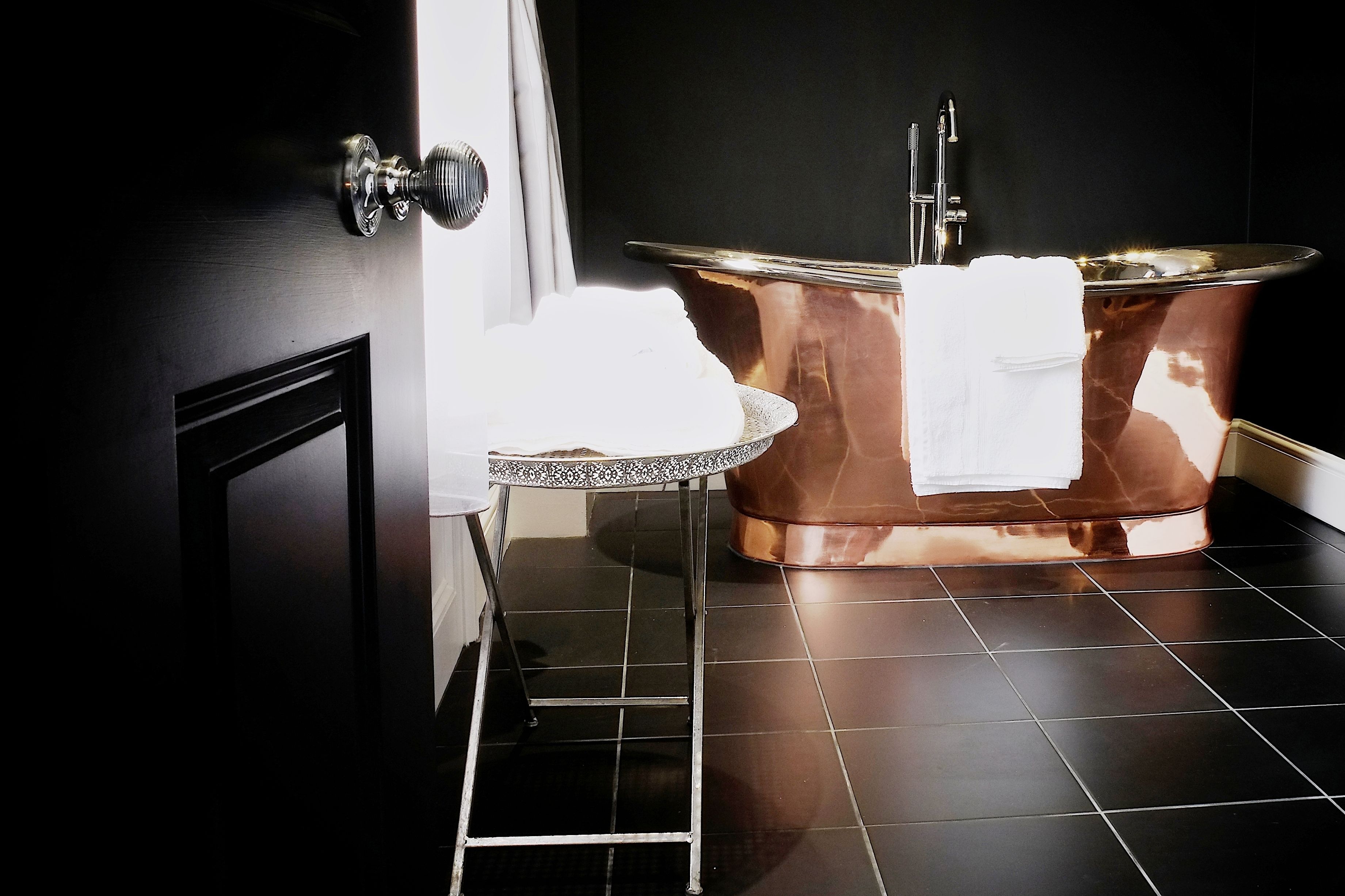 A bathroom with a copper bathtub, a small round table with a white towel, and a door with a silver handle.