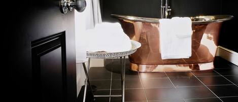 A bathroom with a copper bathtub, a small round table with a white towel, and a door with a silver handle.