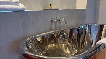 A modern bathroom with a copper bathtub, a mirror, and a towel rack.