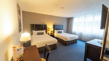 A hotel room with two beds, a desk, a chair, a lamp, and a window with curtains.