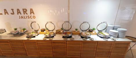 A buffet setup with various food containers and a stack of plates.