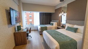 A hotel room with two beds, a desk, a chair, a TV, and a window with a view of buildings. - Hotel Plaza Genova Centro (Guadalajara)