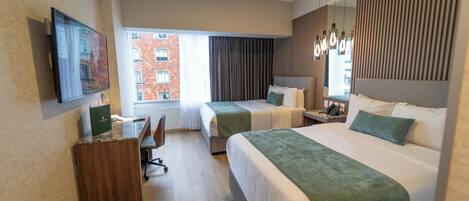 Habitación de hotel con dos camas, un escritorio, una silla, un televisor y una ventana con vista a edificios.