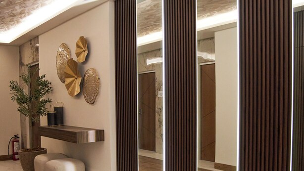 A modern interior with a wooden floor, a wall-mounted shelf with decorative items, and a large mirror reflecting the room. - Hotel Plaza Genova Centro (Guadalajara)