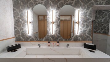 Un baño con un espejo grande, dos lavamanos y un papel tapiz con motivos florales.