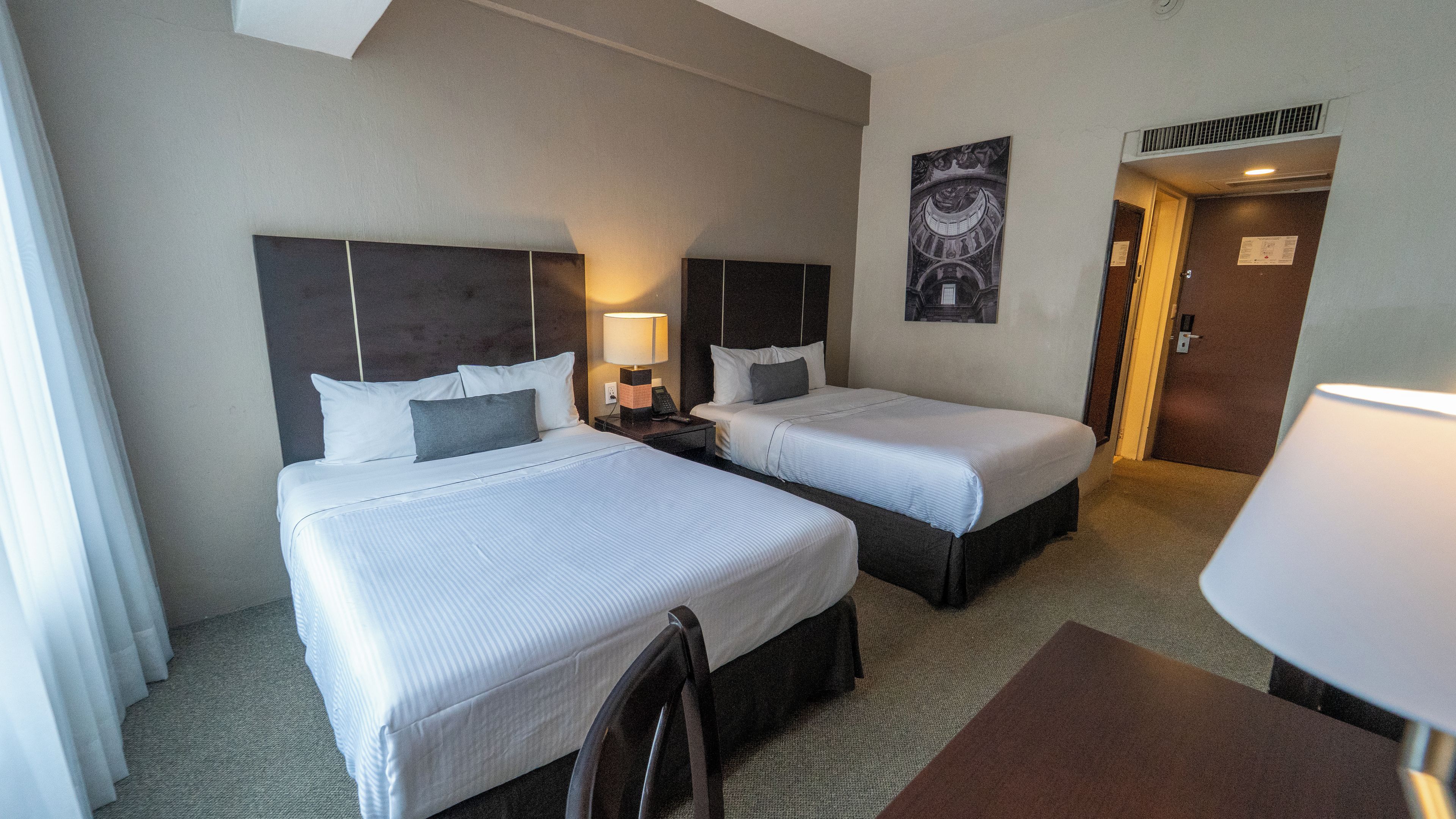 Una habitación de hotel con dos camas, un escritorio, una silla y una lámpara.