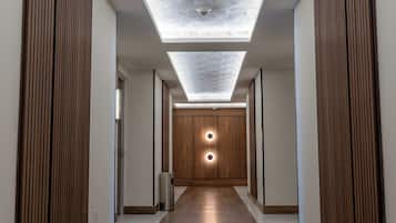 A hallway with a wooden floor, a skylight ceiling, and a circular light fixture at the end.