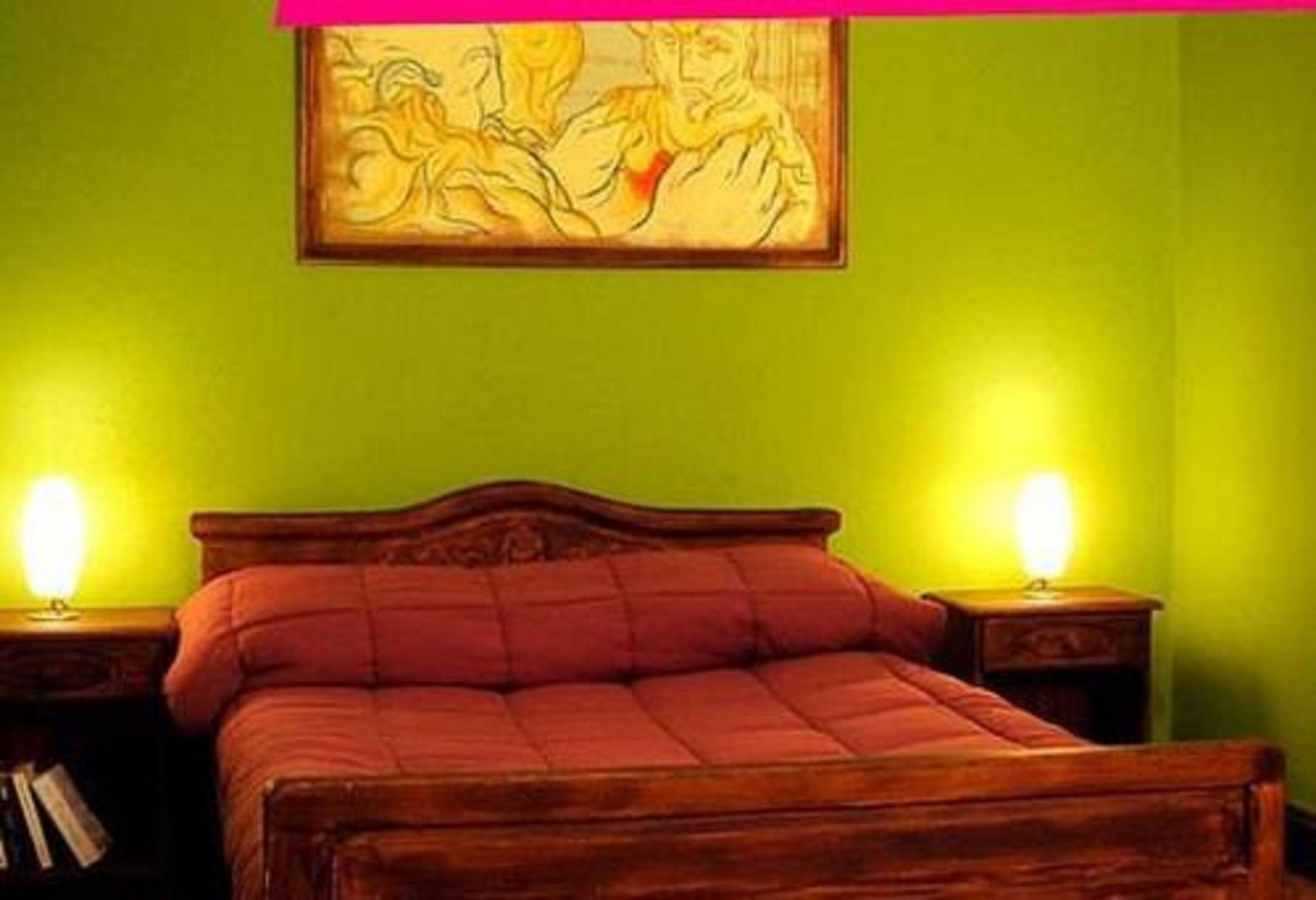 A bed with a wooden headboard, two bedside tables, and a painting above the bed.