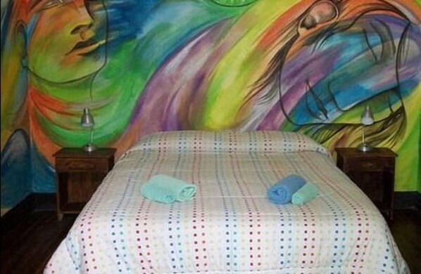 A bedroom with a bed, two bedside tables, and a colorful abstract painting on the wall.