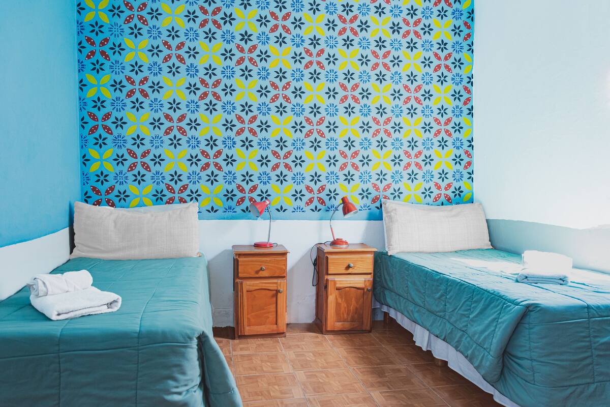 A room with two beds, a patterned wall, and a tiled floor.