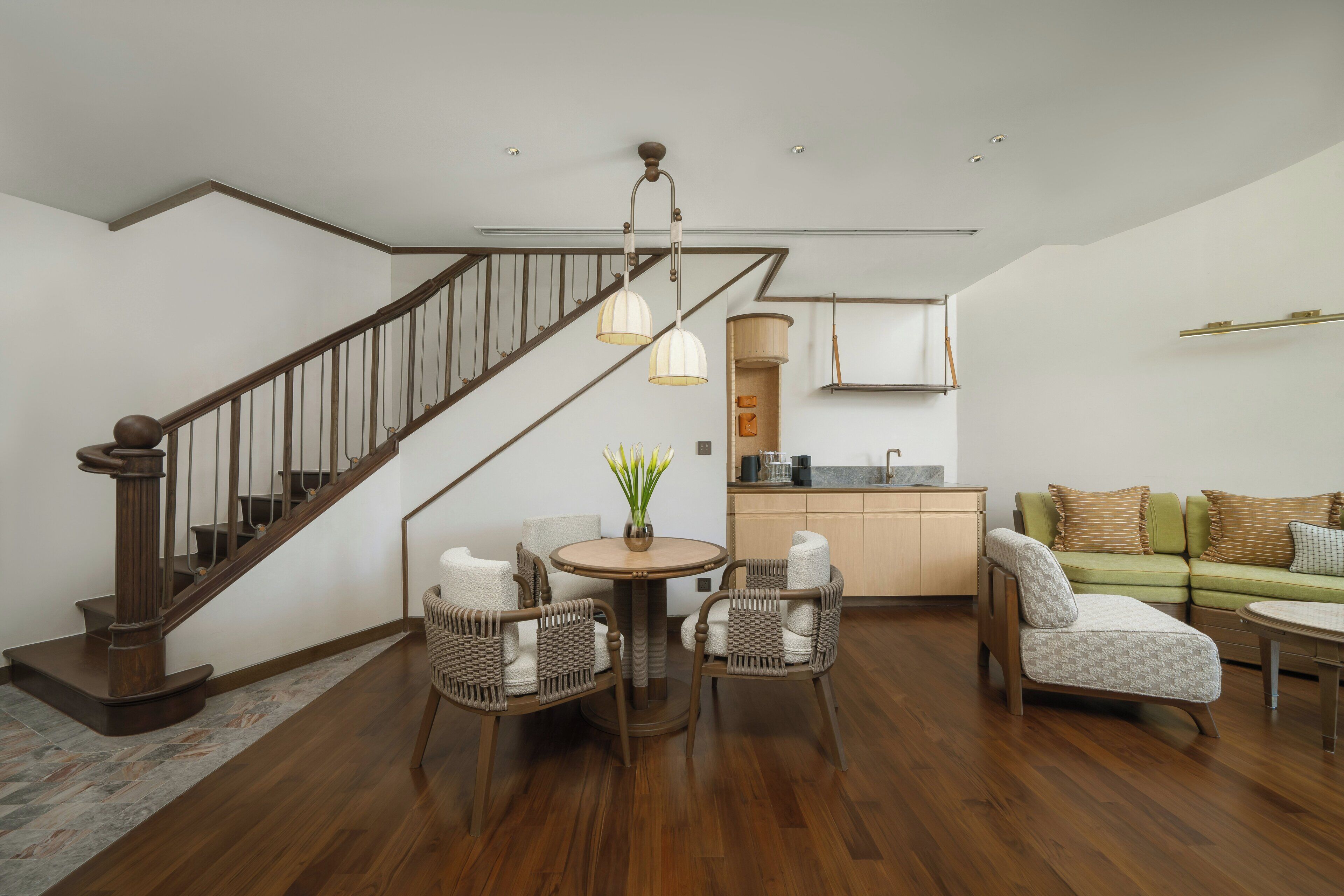 Ein moderner Wohnraum mit einer Holztreppe, Korbmöbeln, einer Küchenzeile und einem grünen Sofa.