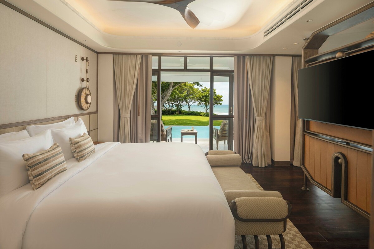 A hotel room with a large bed, a television, and a view of a pool and greenery.