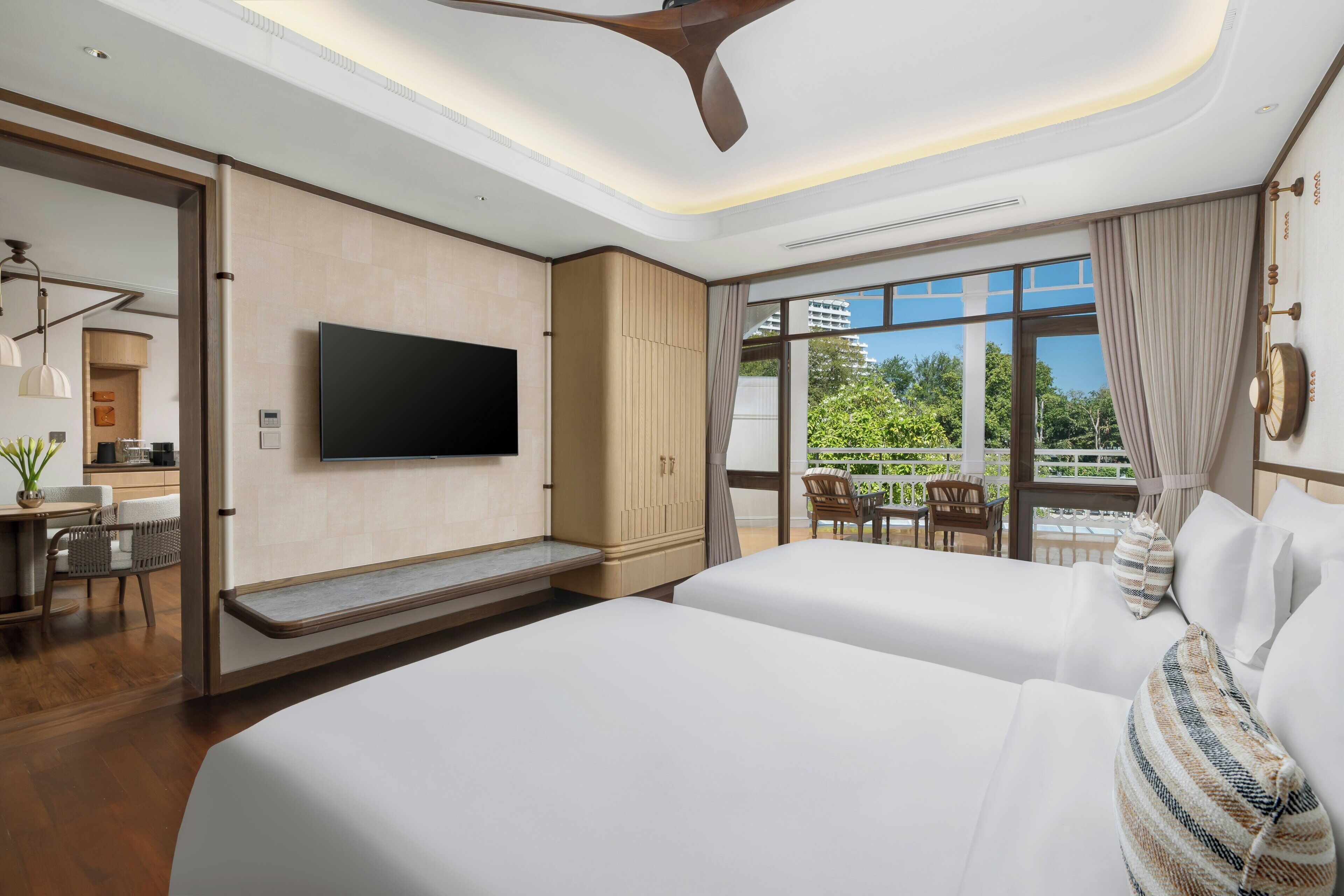 Une chambre d’hôtel avec un grand lit, un téléviseur fixé au mur, un balcon avec vue et un ventilateur de plafond.