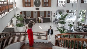 A spacious lobby with a central reception desk, multiple seating areas, and a staircase with wooden railings.