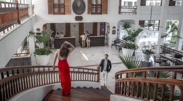 Un amplio vestíbulo con un mostrador de recepción central, varias zonas de estar y una escalera con barandillas de madera.