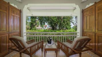 Varanda com estrutura de madeira, com duas cadeiras e uma mesa, com vista para um jardim exuberante e um edifício ao longe.
