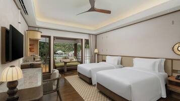 A hotel room with two beds, a desk with a lamp, a TV, and a view of a pool and greenery.