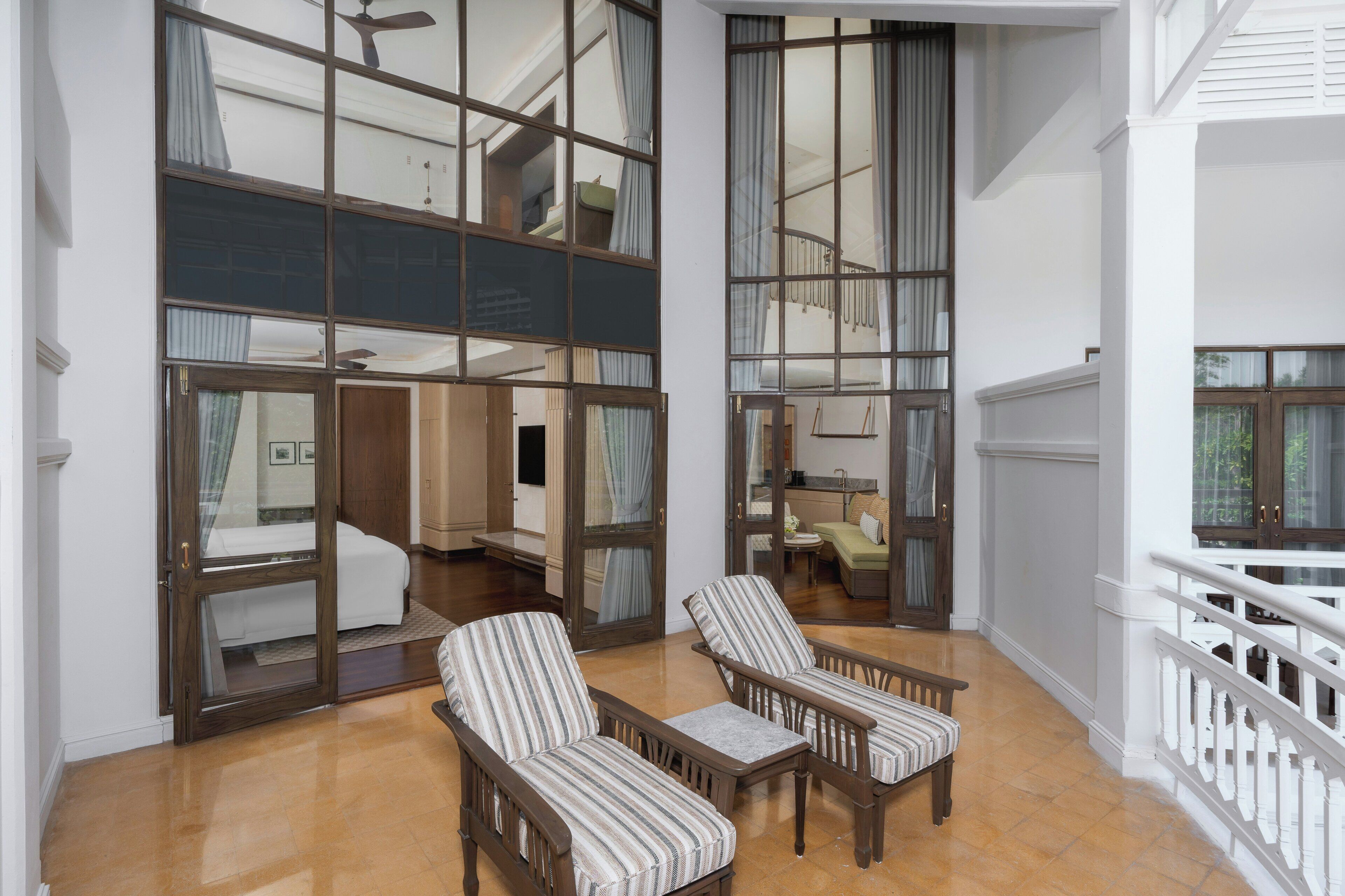 Un balcon spacieux avec deux fauteuils à rayures, un banc en bois et une vue sur l’intérieur.