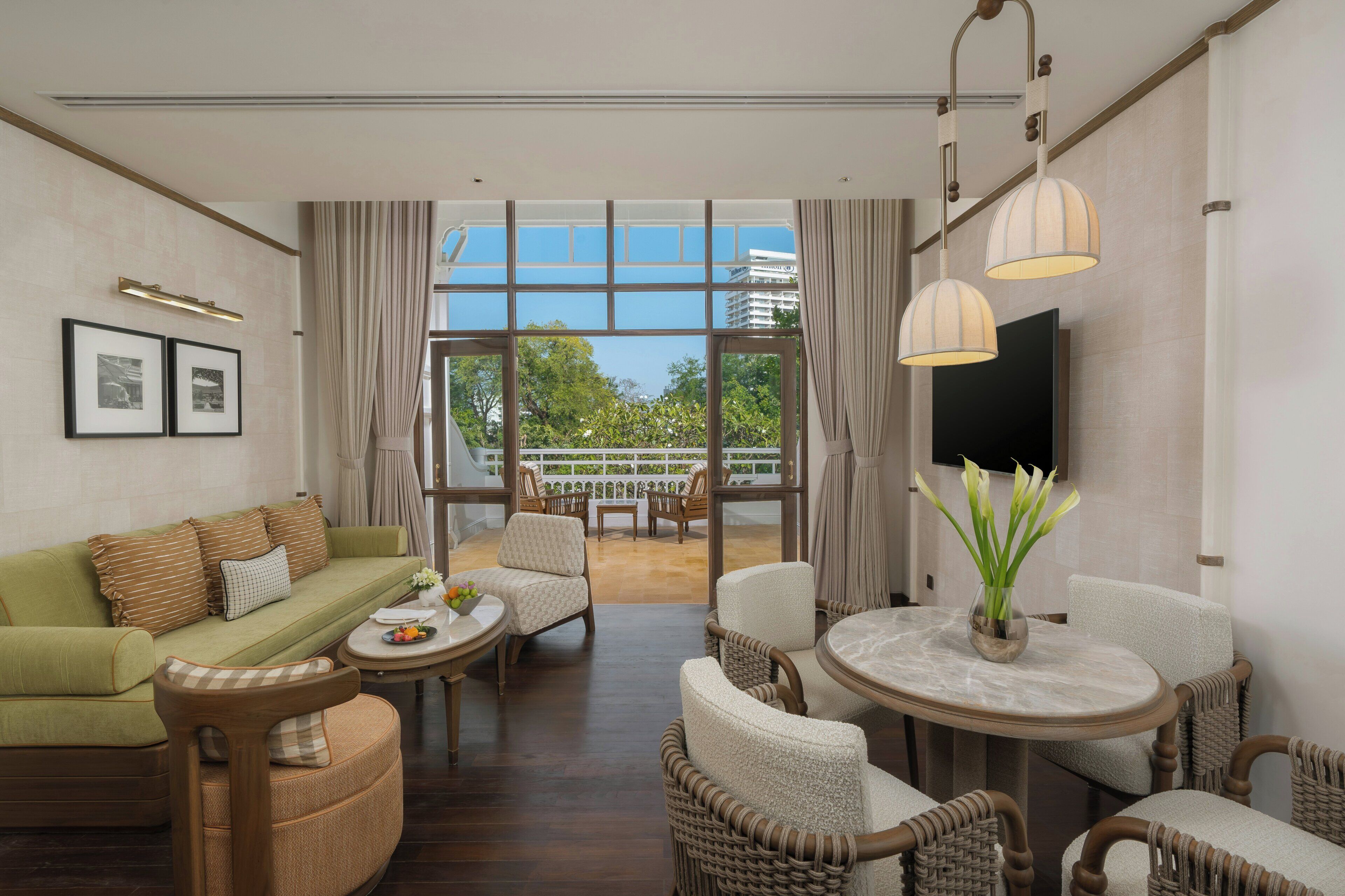 A hotel room with a sofa, chairs, a dining table, a TV, and a balcony with a view.