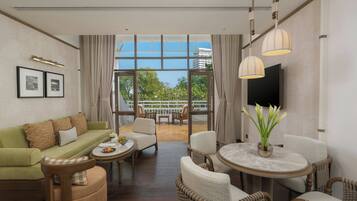 A hotel room with a sofa, chairs, a dining table, a TV, and a balcony with a view.