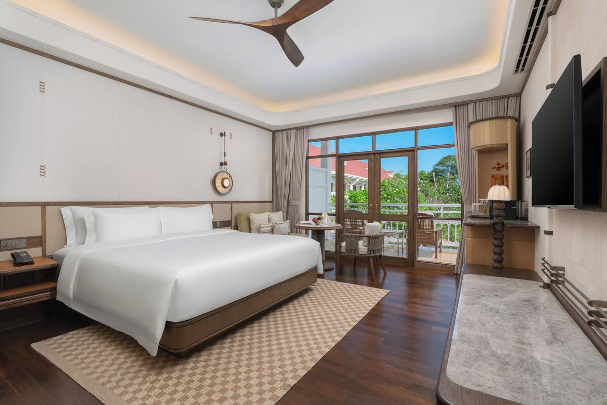 Ein Hotelzimmer mit einem großen Bett, einem Schreibtisch mit Stuhl, einem Fernseher und einem Balkon mit Aussicht.