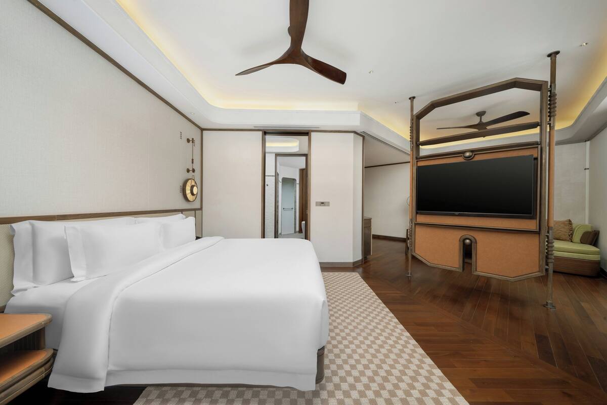 Ein Hotelzimmer mit einem großen Bett, einem Fernseher, einem Deckenventilator und einem karierten Teppich.
