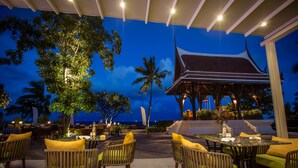An outdoor dining area with wooden chairs and tables, a covered pavilion, and a view of the sea. - Centara Grand Beach Resort Hua Hin (Hua Hin)
