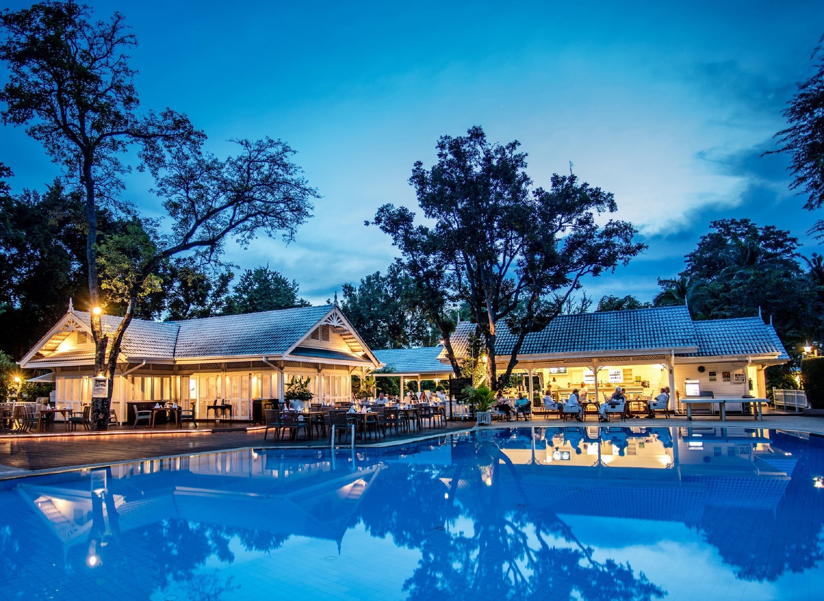 A poolside area with a reflection pool, wooden deck, and two buildings with tiled roofs.