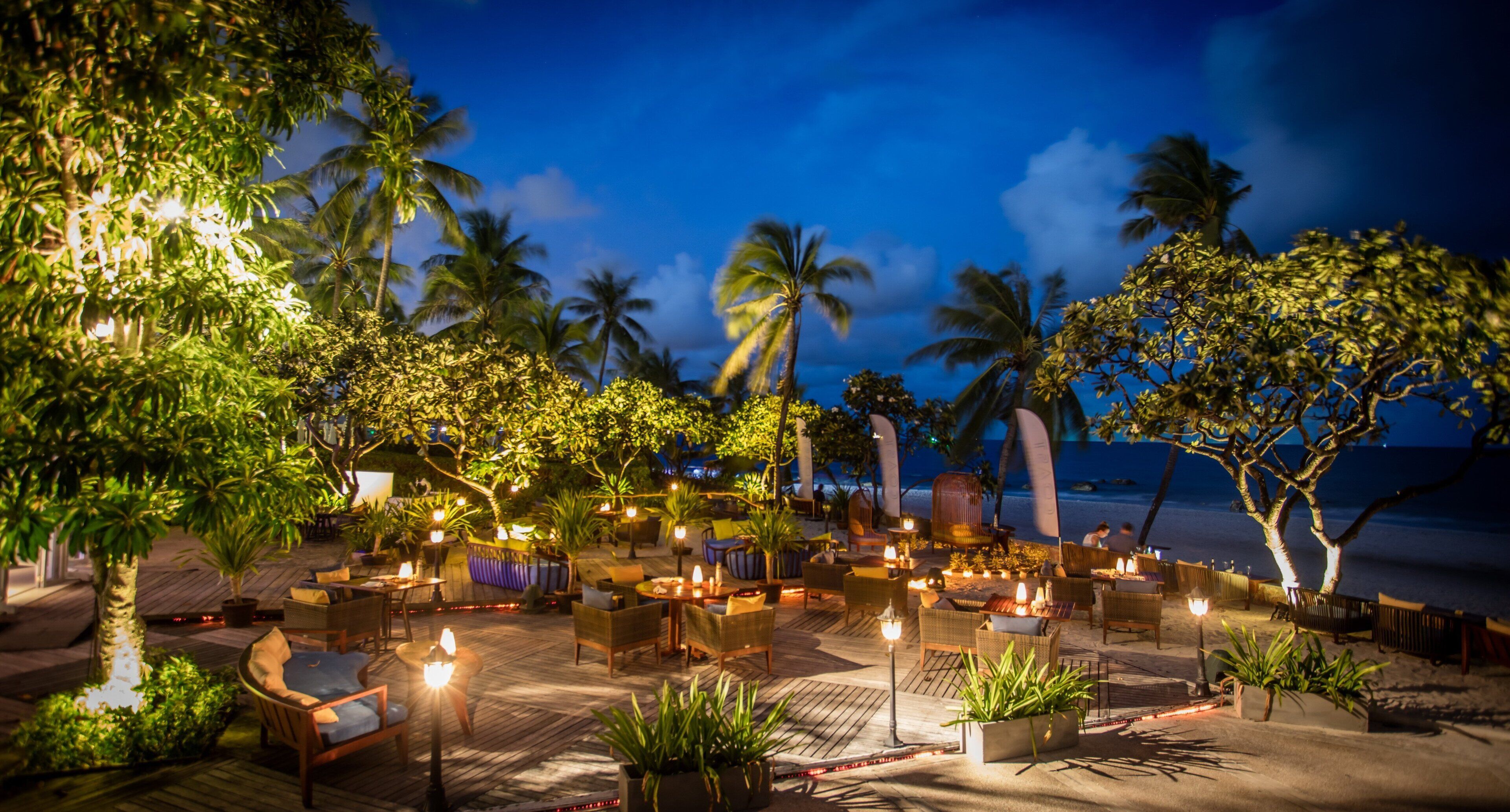 An outdoor lounge area with wooden furniture, potted plants, and string lights.