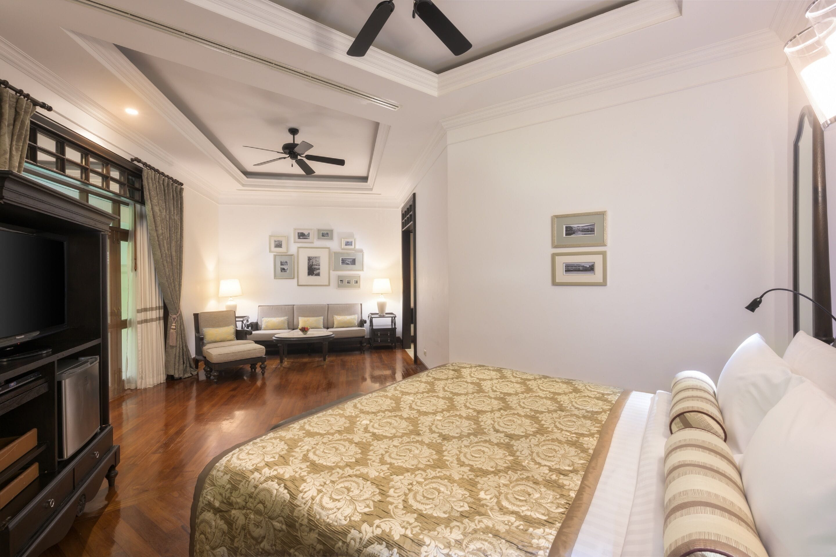 A hotel room with a large bed, a TV, a ceiling fan, and a seating area with a sofa and chairs.