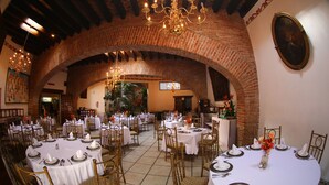 Een restaurant met ronde tafels, witte tafellinnen en gouden stoelen.