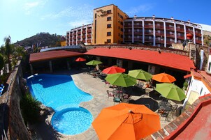 Un hotel con piscina, mobiliario exterior con sombrillas y vistas a un paisaje montañoso.
