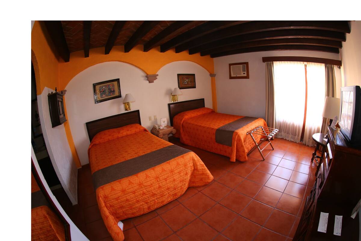 A room with two beds, wooden beams on the ceiling, a tiled floor, and a television on a wooden cabinet.