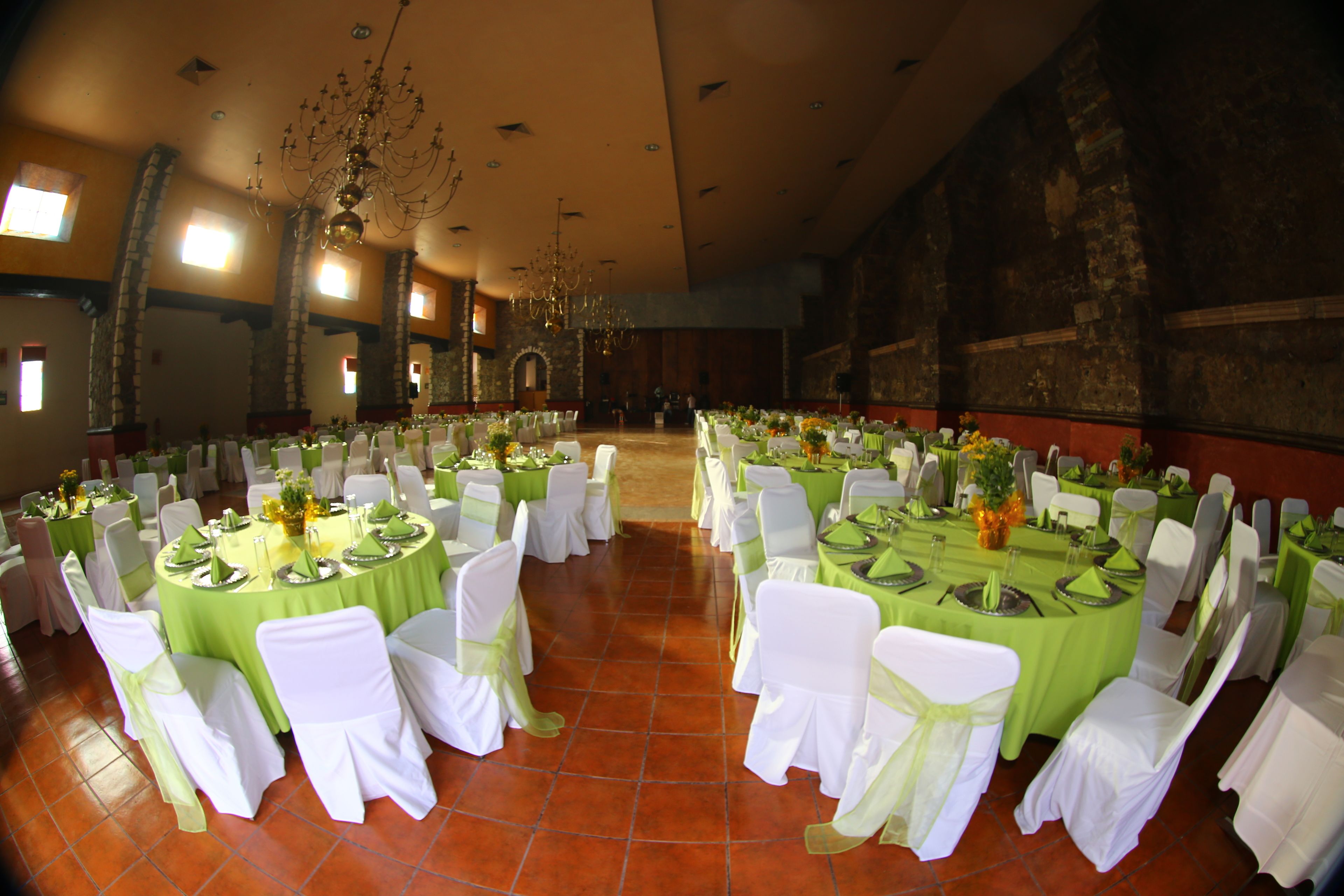 Un salón de banquetes con mesas redondas, sillas blancas y manteles verdes.