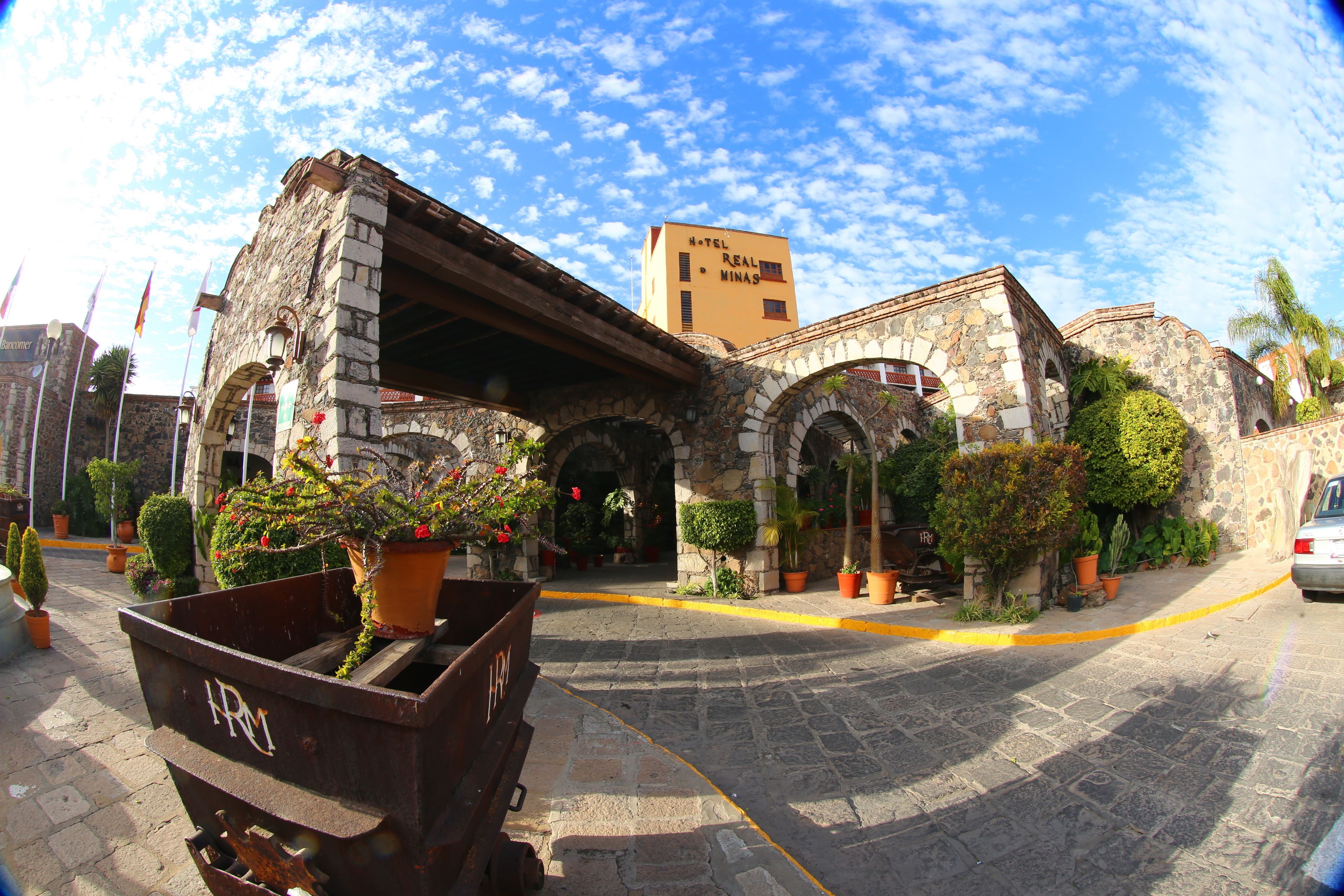 Un edificio de piedra histórico con una entrada en arco, un letrero que dice 'Hotel Real Minas' y plantas en macetas alrededor de la entrada.