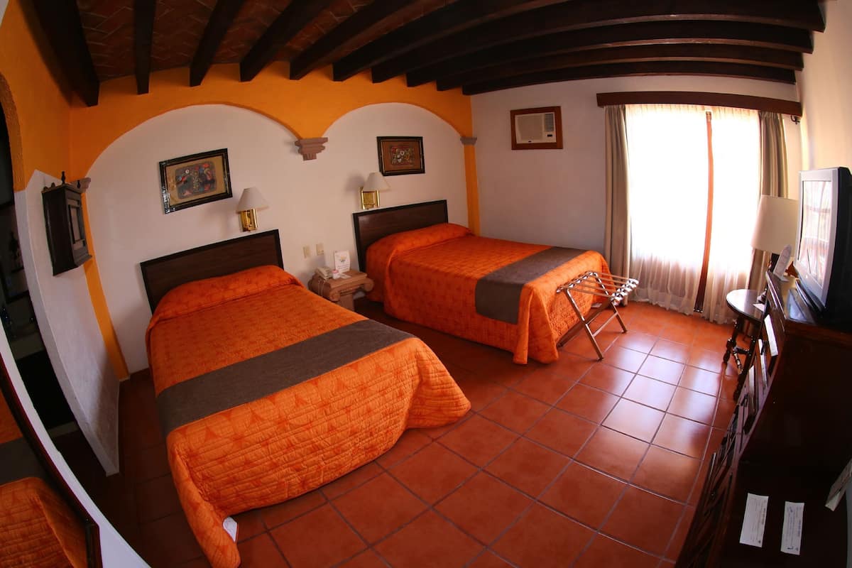 A room with two beds, a television, a desk, and a window with curtains.