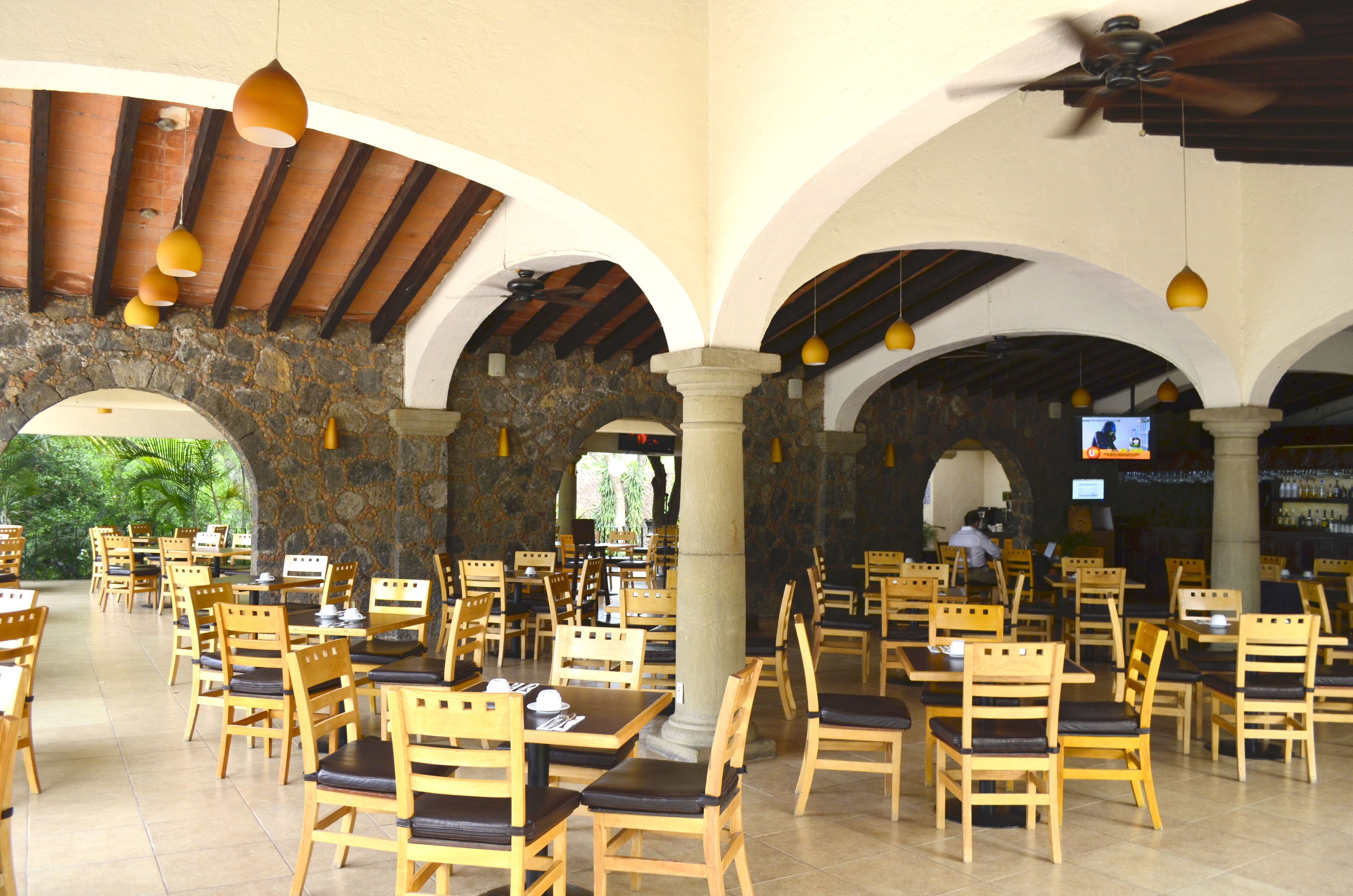 Un restaurante con mesas y sillas de madera, paredes de piedra y un ventilador de techo.