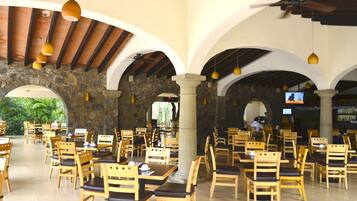 Un restaurante con mesas y sillas de madera, paredes de piedra y un ventilador de techo.