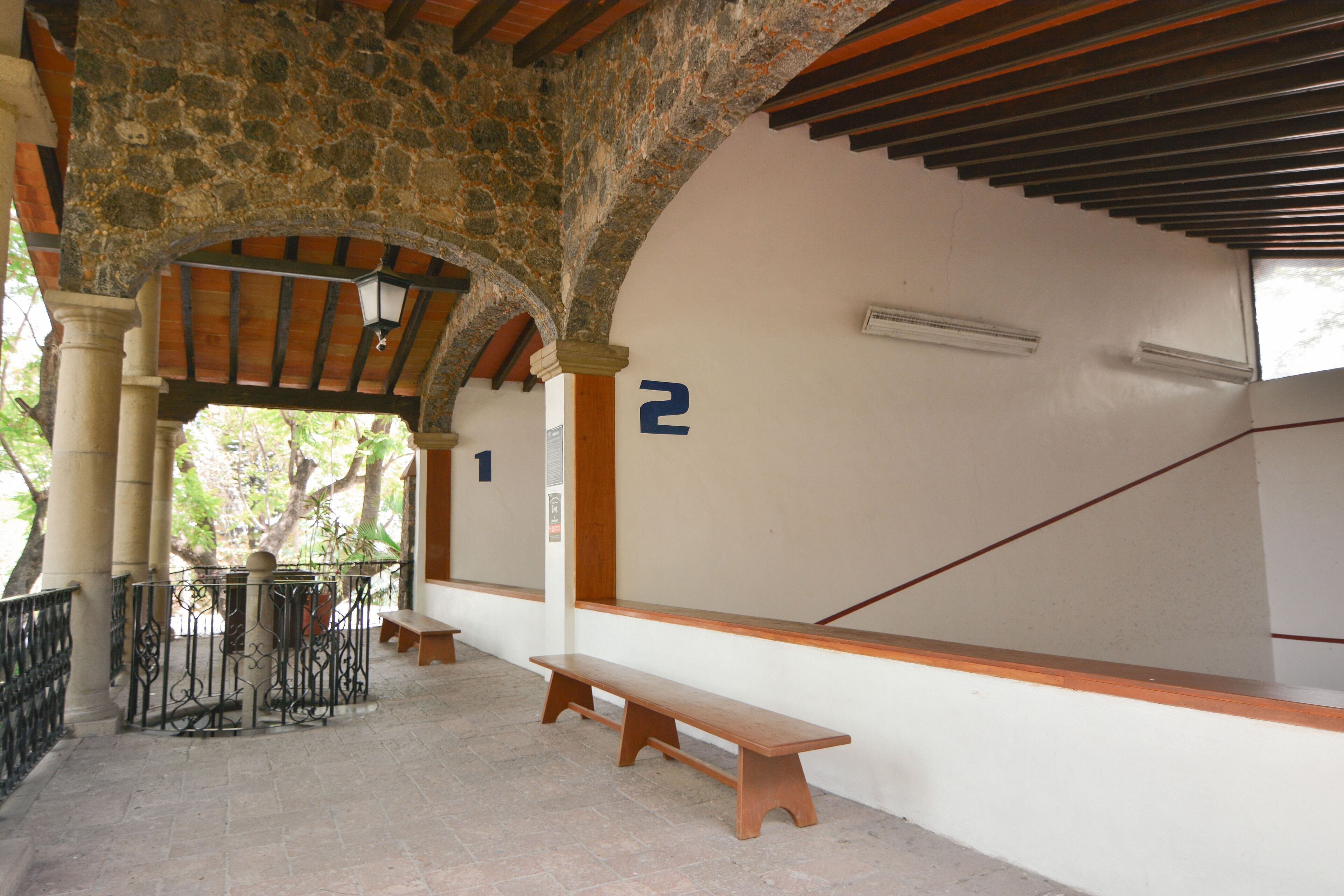 A covered outdoor area with stone columns, wooden benches, and a staircase with numbers indicating levels.