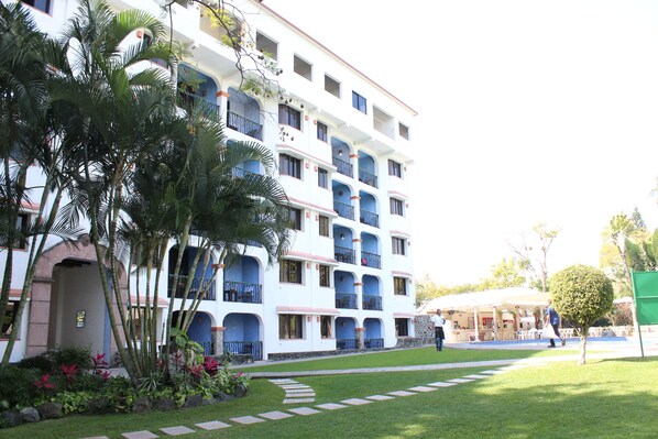 Un hôtel à plusieurs étages doté de balcons, d’une pelouse bien entretenue et d’un espace piscine.