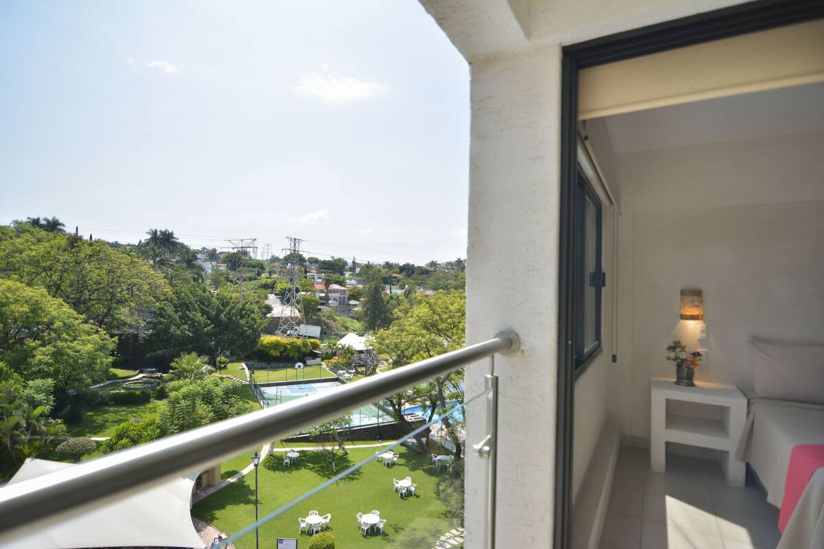 Ein Balkon mit Blick auf einen angelegten Garten und ein Schwimmbad.