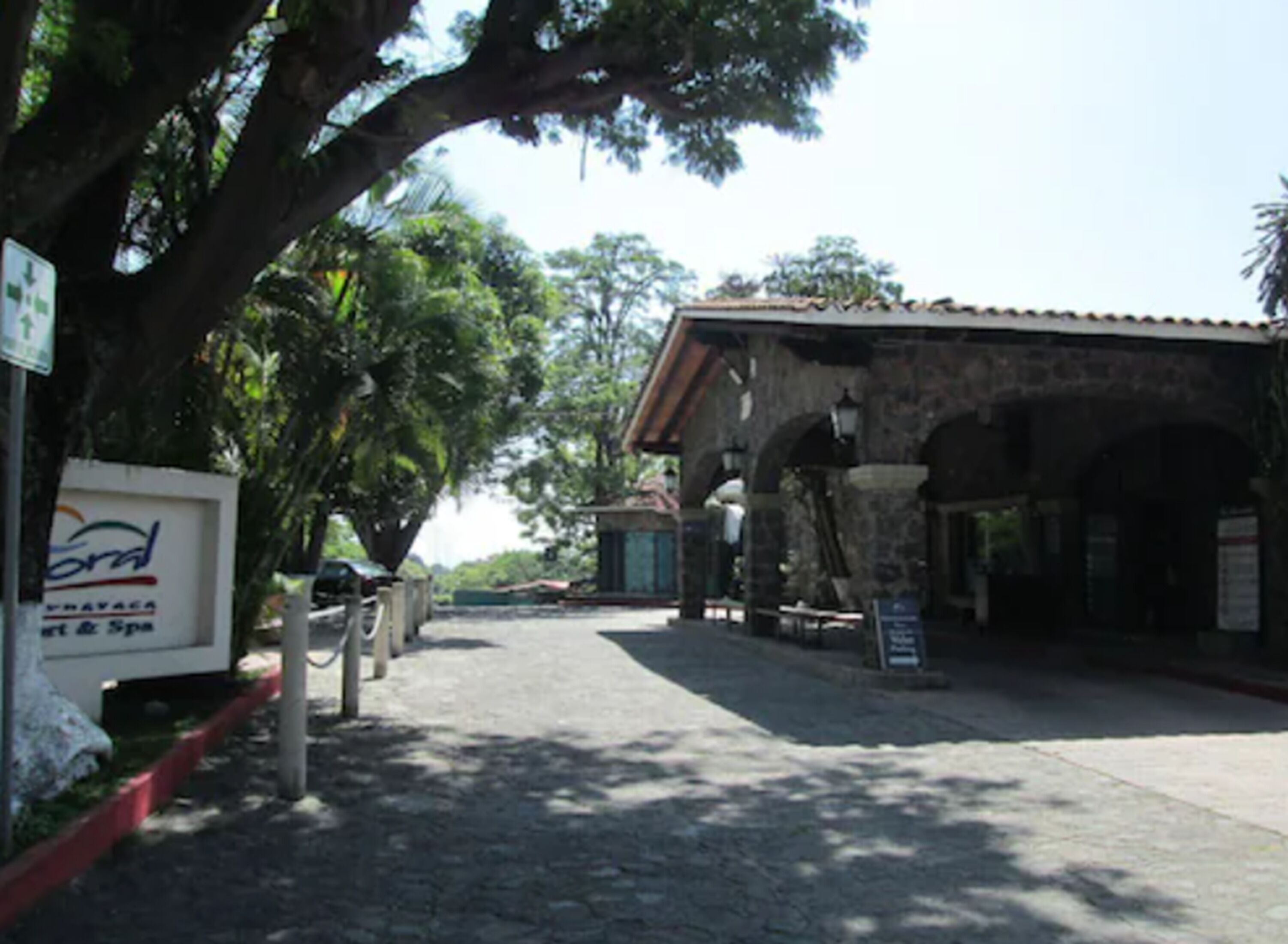 A street with a sign for Ford, a stone building with a tiled roof, and a tree-lined path.